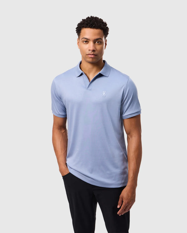 A man in a Psycho Bunny MENS BROADWAY MERCERIZED PIMA POLO SHIRT (B6K891D200), light blue with a small white logo, stands against a plain white background. Made from durable, lustrous mercerized Pima cotton, he is paired with black pants and has short curly hair and a neutral expression.