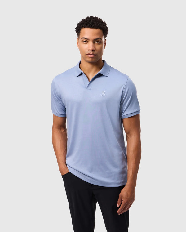 A man in a Psycho Bunny MENS BROADWAY MERCERIZED PIMA POLO SHIRT (B6K891D200), light blue with a small white logo, stands against a plain white background. Made from durable, lustrous mercerized Pima cotton, he is paired with black pants and has short curly hair and a neutral expression.