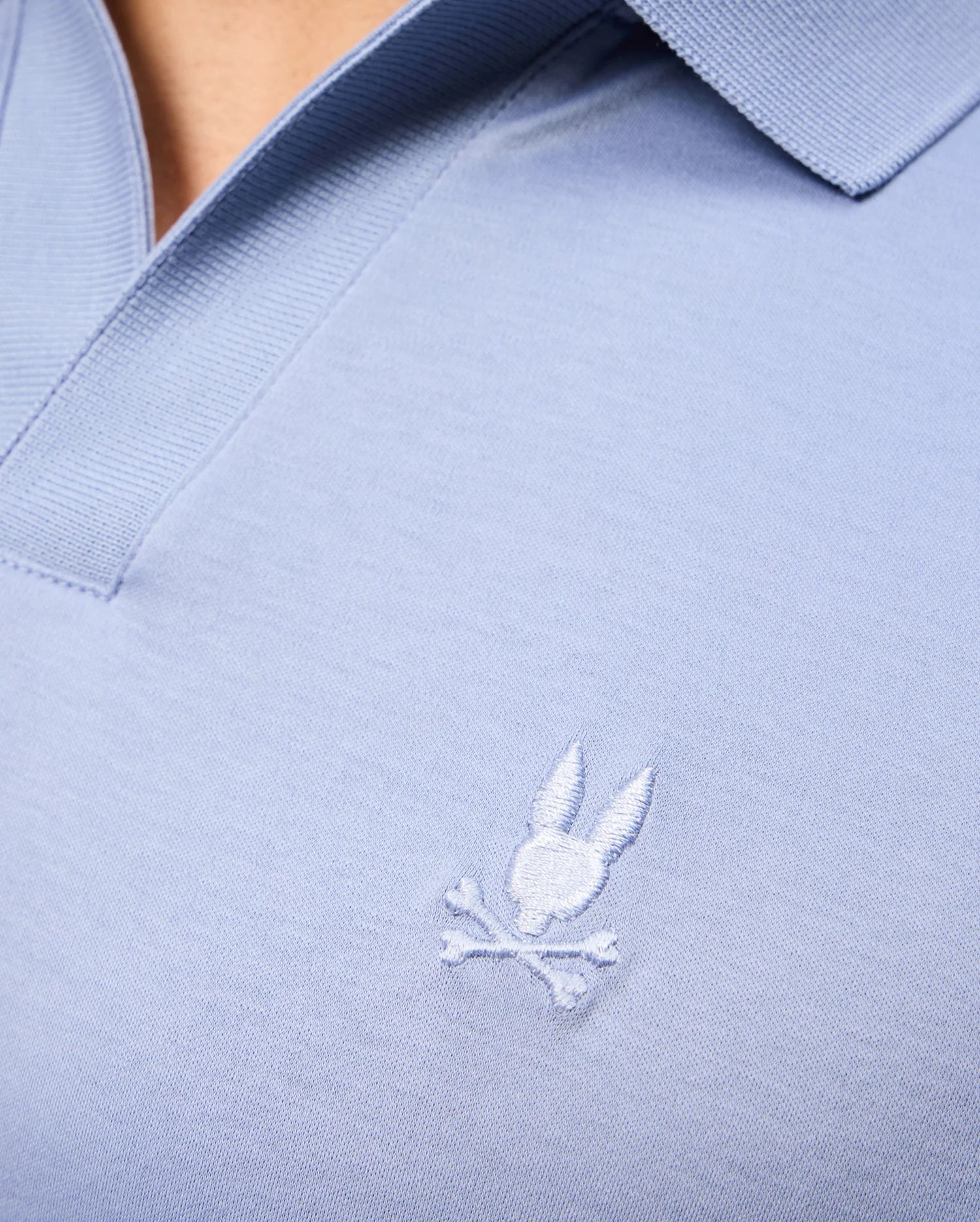 Close-up of the Psycho Bunny MENS BROADWAY MERCERIZED PIMA POLO SHIRT - B6K891D200 in light blue, made from mercerized Pima cotton for lasting shine. It has a small embroidered rabbit head with crossed bones and a ribbed collar.