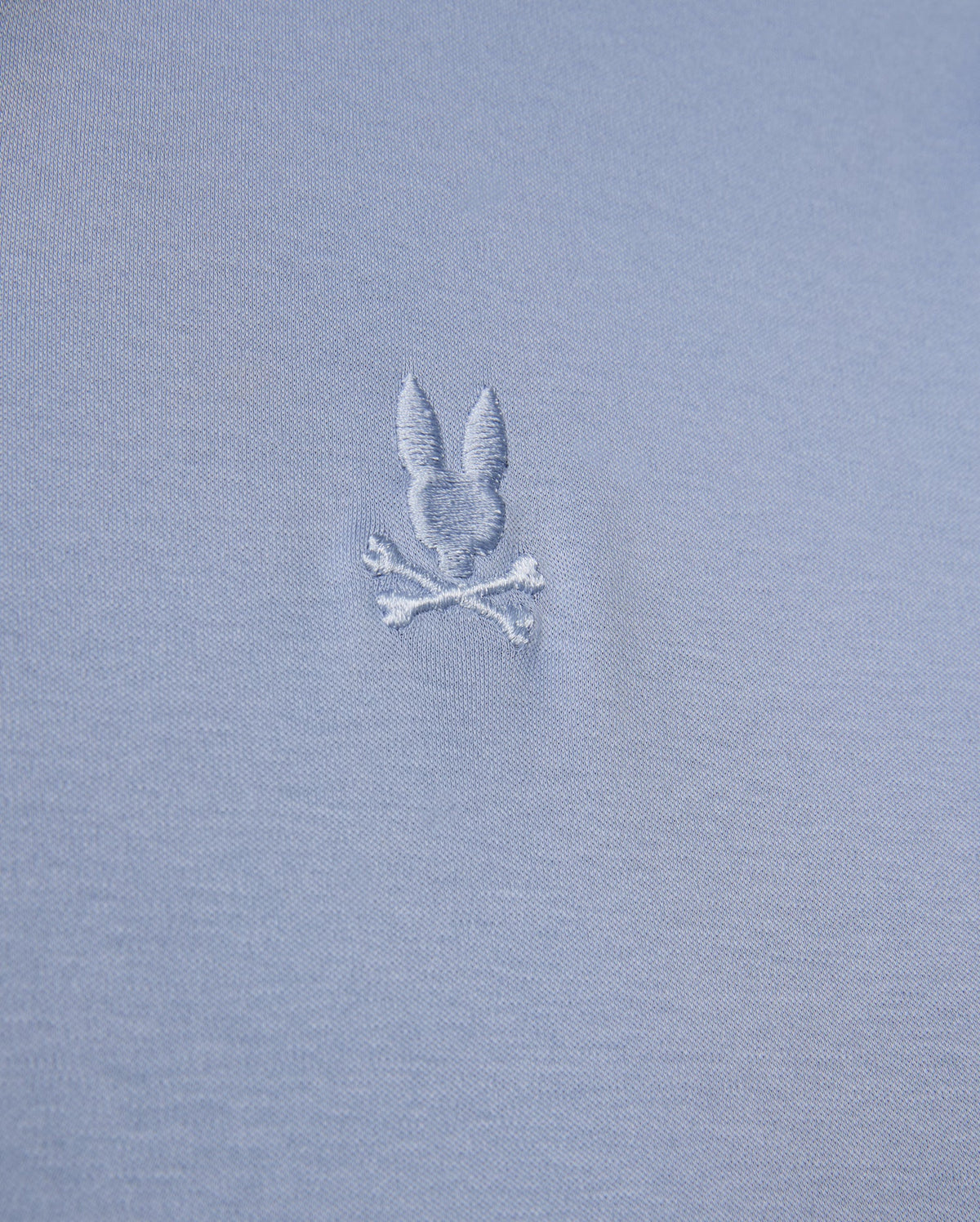 The MENS BROADWAY MERCERIZED PIMA POLO SHIRT by Psycho Bunny showcases a close-up of durable gray luster fabric with an embroidered design featuring a bunny head above two crossed bones.