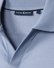 Close-up of the MENS BROADWAY MERCERIZED PIMA POLO SHIRT - B6K891D200 in light blue, featuring the "Psycho Bunny" black label at the collar with a bunny emblem. The durable lustre of the mercerized Pima cotton enhances its texture, highlighting stitching details for elegance and resilience.
