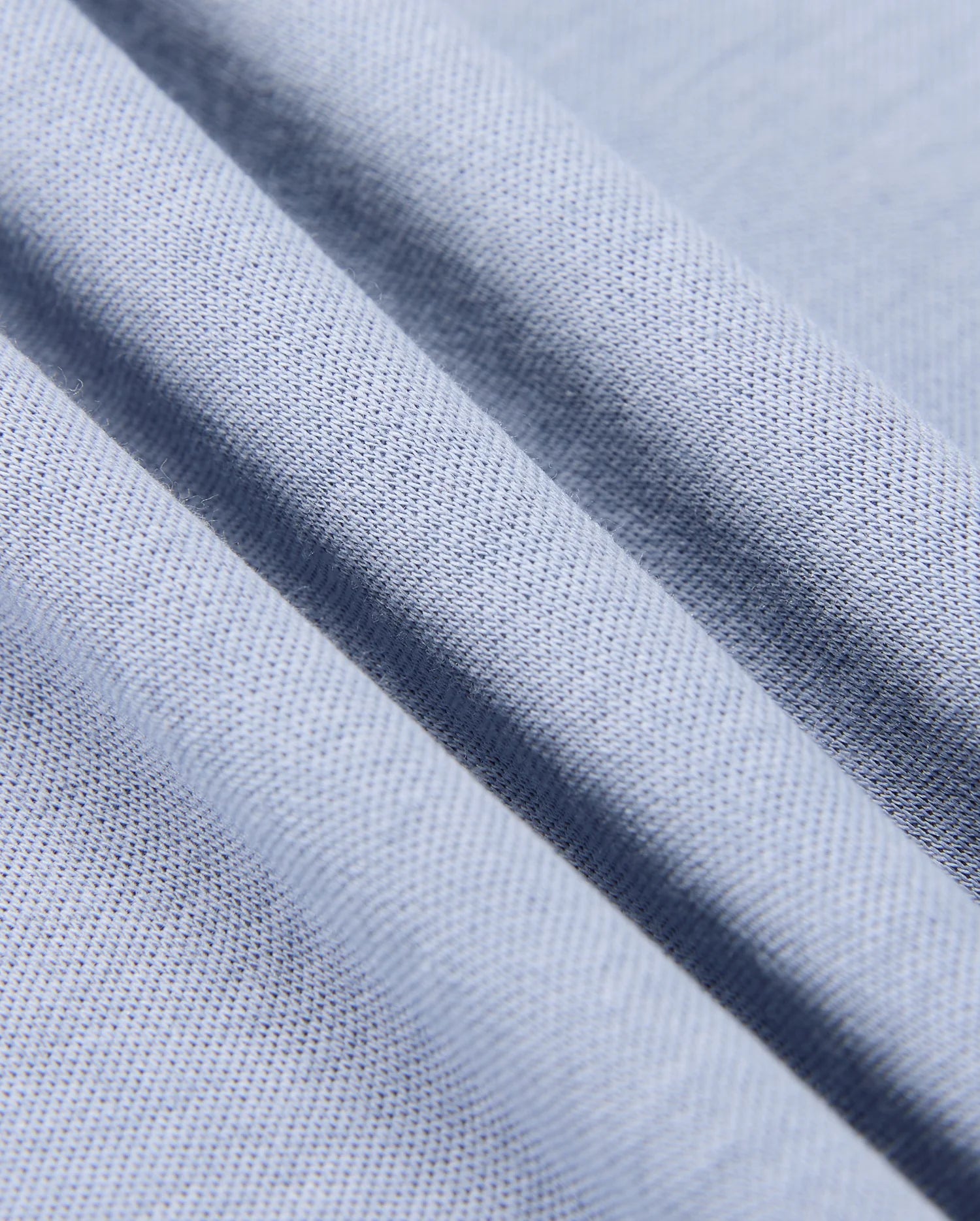 Close-up of the Psycho Bunny Men's Broadway Mercerized Pima Polo Shirt (B6K891D200) in light blue with diagonal folds, highlighting its lustrous and durable weave. The fine, evenly spaced threads accentuate the softness typical of mercerized Pima cotton.
