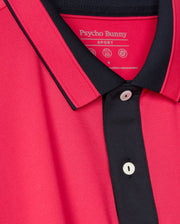 A close-up of the versatile casual pink Bellevue Sport Polo Shirt by Psycho Bunny, showcasing its black trim on the collar and button placket with visible white buttons. The breathable performance polo features a tag that indicates the brand name "Psycho Bunny.