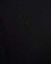 Close-up of the Psycho Bunny MENS JAMES PREMIUM PIQUE POLO SHIRT, crafted from durable black textured Pima cotton fabric and showcasing an embroidered design of a bunny head above crossed bones.