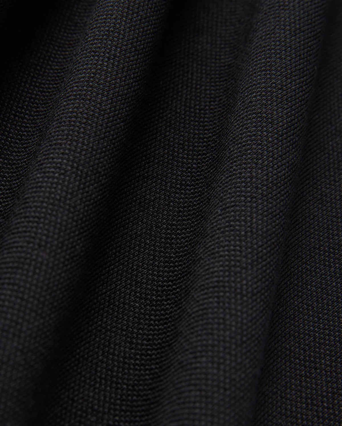 Close-up of the black textured fabric from the Psycho Bunny MENS JAMES PREMIUM PIQUE POLO SHIRT - B6K945D200, featuring a visible weave pattern. The surface, crafted from premium finer yarn, forms soft, undulating folds that highlight its thickness and quality.