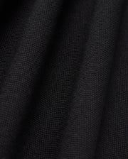 Close-up of the black textured fabric from the Psycho Bunny MENS JAMES PREMIUM PIQUE POLO SHIRT - B6K945D200, featuring a visible weave pattern. The surface, crafted from premium finer yarn, forms soft, undulating folds that highlight its thickness and quality.