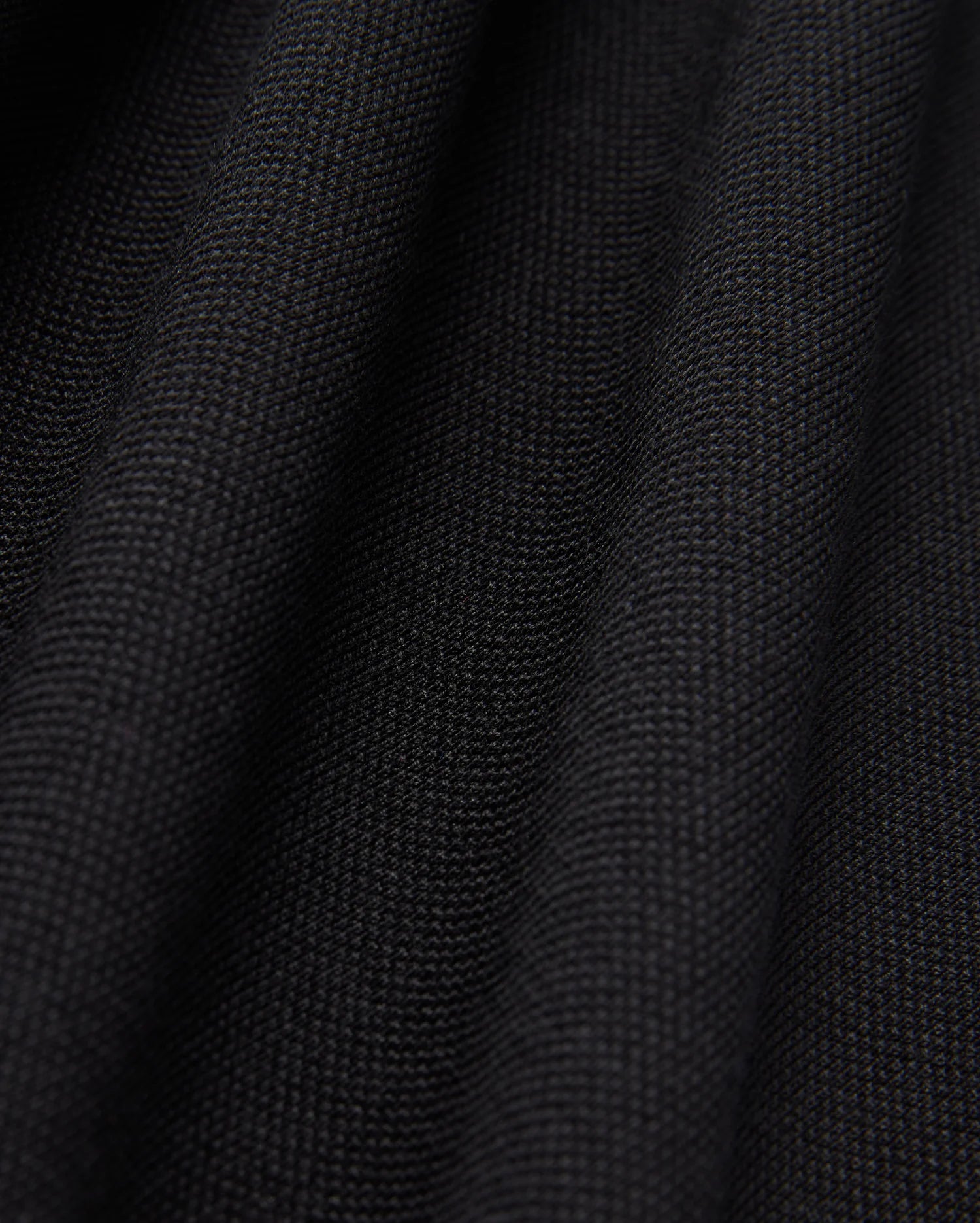Close-up of the black textured fabric from the Psycho Bunny MENS JAMES PREMIUM PIQUE POLO SHIRT - B6K945D200, featuring a visible weave pattern. The surface, crafted from premium finer yarn, forms soft, undulating folds that highlight its thickness and quality.