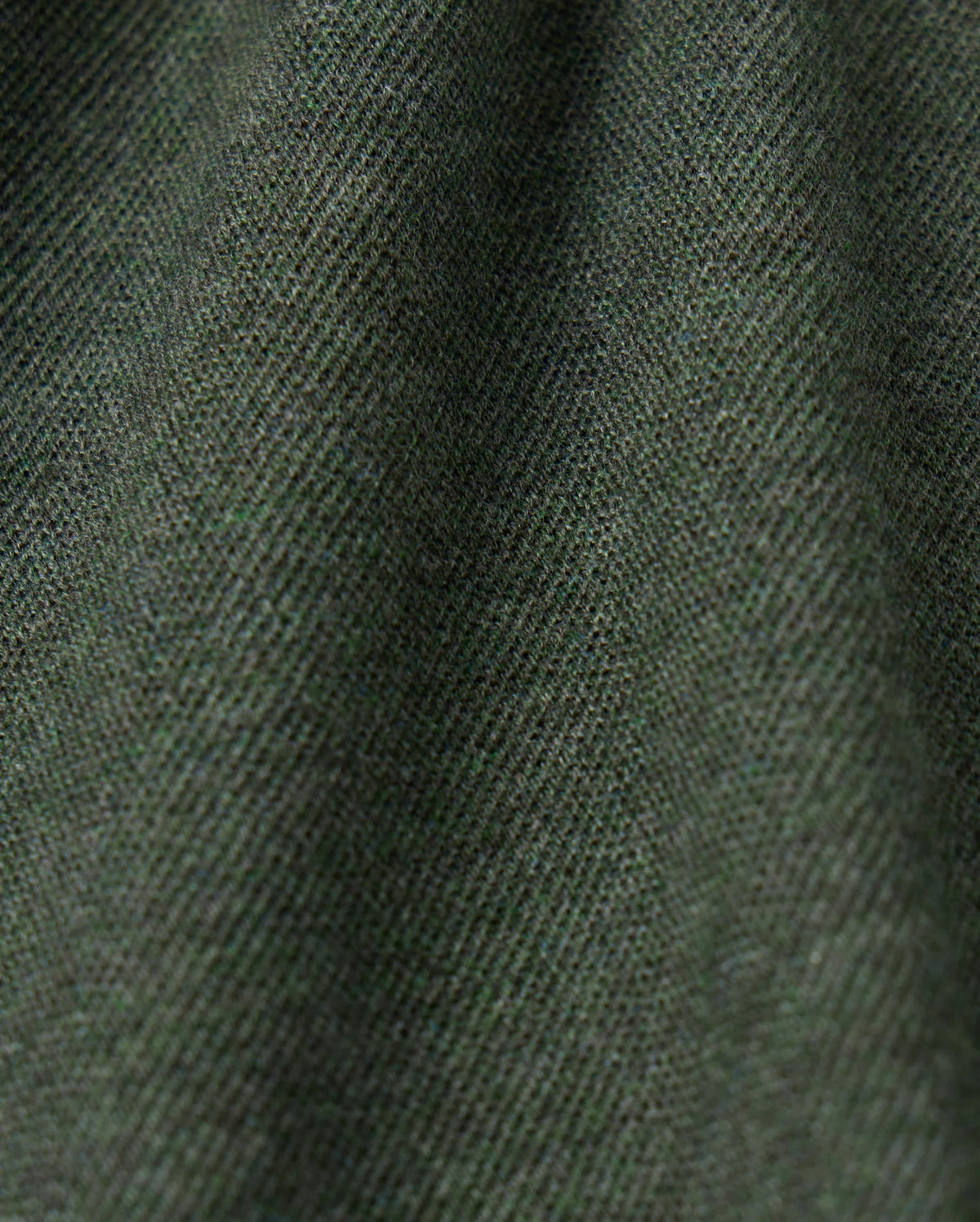 Close-up image of the MENS JAMES PREMIUM PIQUE POLO SHIRT - B6K945D200 by Psycho Bunny, showcasing its dark green premium fabric with a fine diagonal weave pattern that creates a textured appearance. The lighting accentuates the subtle variations in this high-quality polo for men.