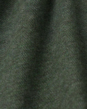 Close-up image of the MENS JAMES PREMIUM PIQUE POLO SHIRT - B6K945D200 by Psycho Bunny, showcasing its dark green premium fabric with a fine diagonal weave pattern that creates a textured appearance. The lighting accentuates the subtle variations in this high-quality polo for men.