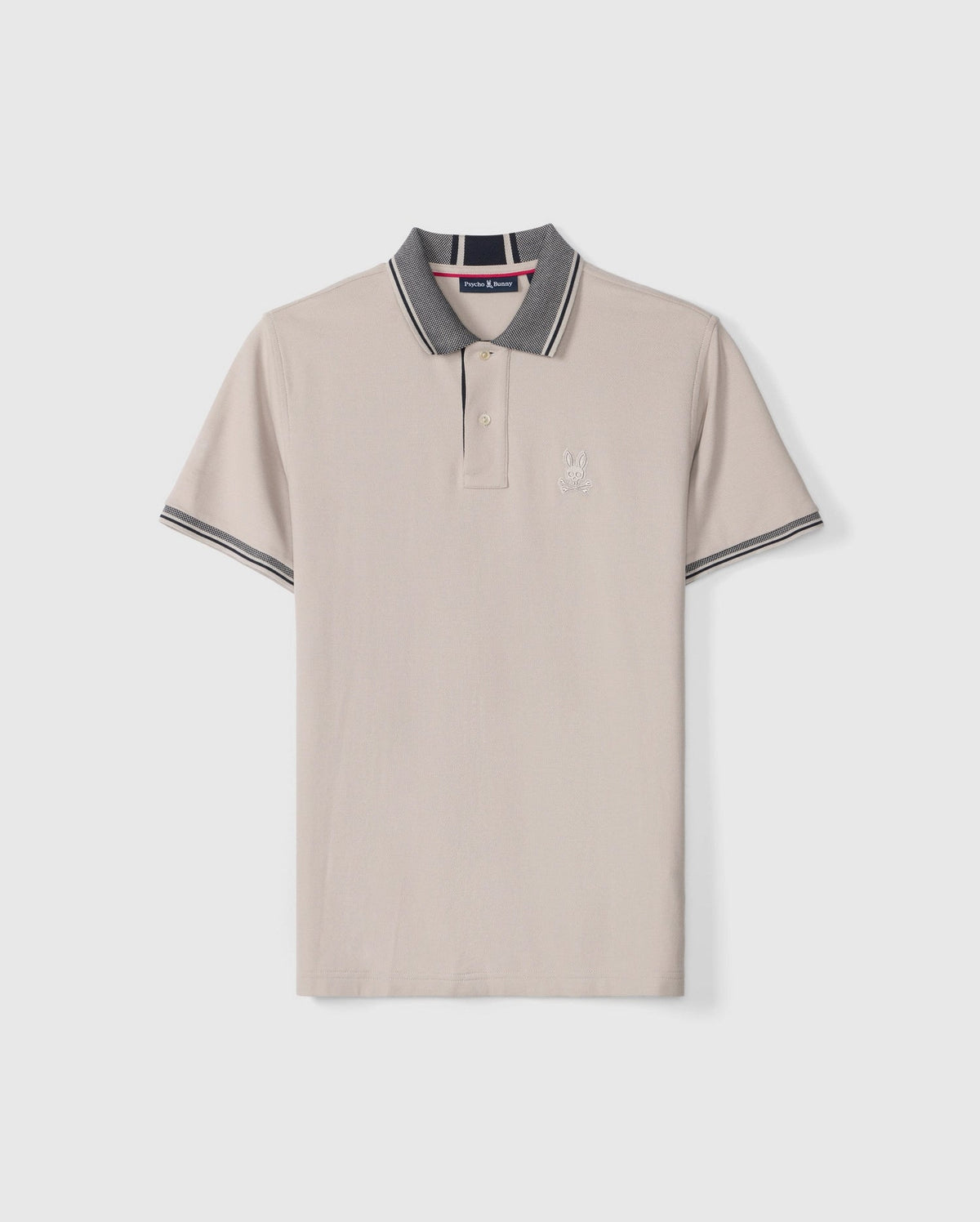 Introducing the MENS MALTON PIQUE POLO SHIRT - B6K950D200 by Psycho Bunny: This light beige Pima cotton polo shirt features short sleeves, a collar adorned with dark gray and white stripes along the edges, and a striking diamond pique pattern. Psycho Bunny's signature embroidered rabbit logo graces the left chest, while the brand's tag is visible inside the collar.