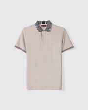 Introducing the MENS MALTON PIQUE POLO SHIRT - B6K950D200 by Psycho Bunny: This light beige Pima cotton polo shirt features short sleeves, a collar adorned with dark gray and white stripes along the edges, and a striking diamond pique pattern. Psycho Bunny's signature embroidered rabbit logo graces the left chest, while the brand's tag is visible inside the collar.