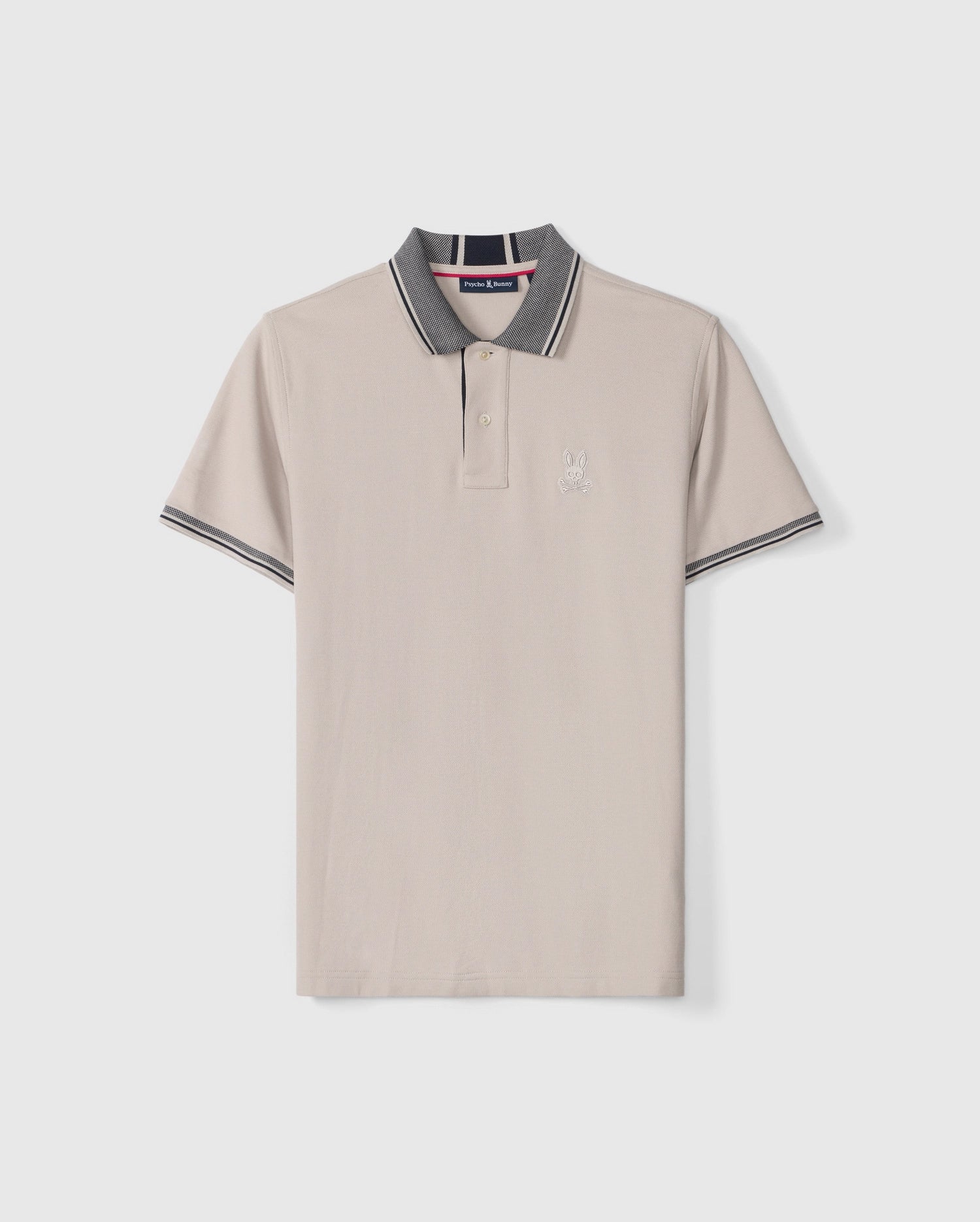 Introducing the MENS MALTON PIQUE POLO SHIRT - B6K950D200 by Psycho Bunny: This light beige Pima cotton polo shirt features short sleeves, a collar adorned with dark gray and white stripes along the edges, and a striking diamond pique pattern. Psycho Bunny's signature embroidered rabbit logo graces the left chest, while the brand's tag is visible inside the collar.