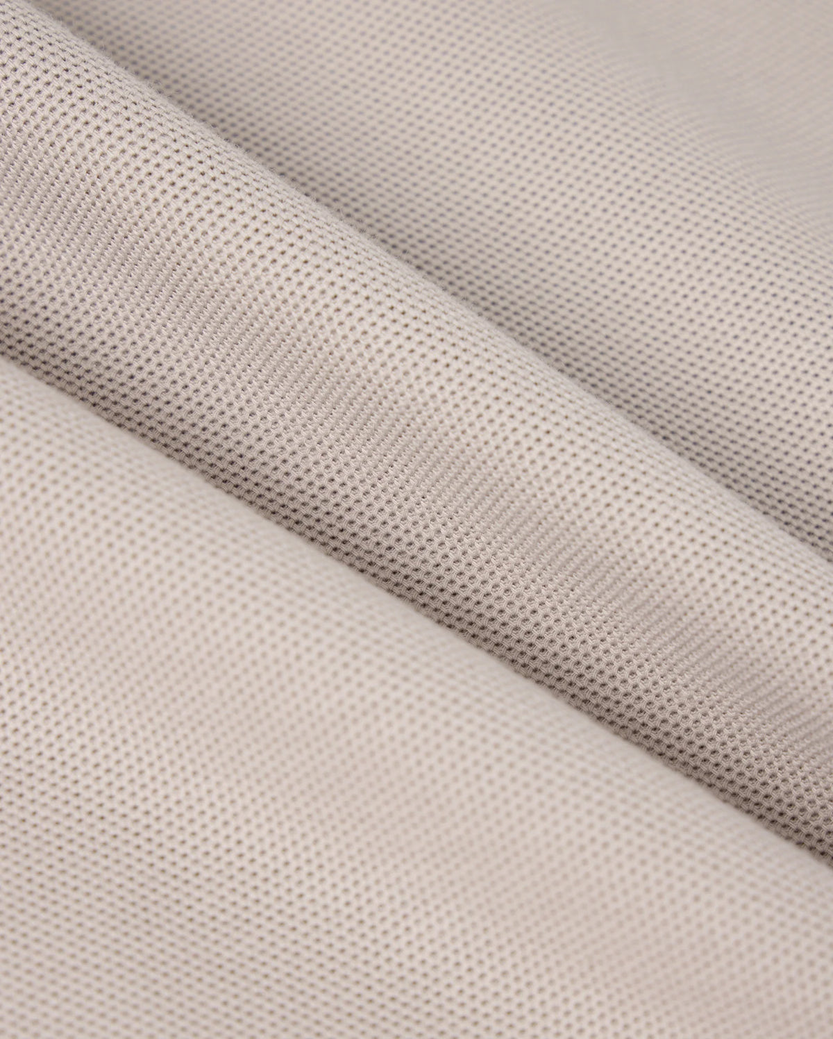 Close-up of a piece of light grey woven fabric with a fine, smooth texture. The fabric is draped to create gentle, diagonal folds, highlighting its soft and pliable nature, reminiscent of the exquisite feel found in Psycho Bunny's MENS MALTON PIQUE POLO SHIRT - B6K950D200.