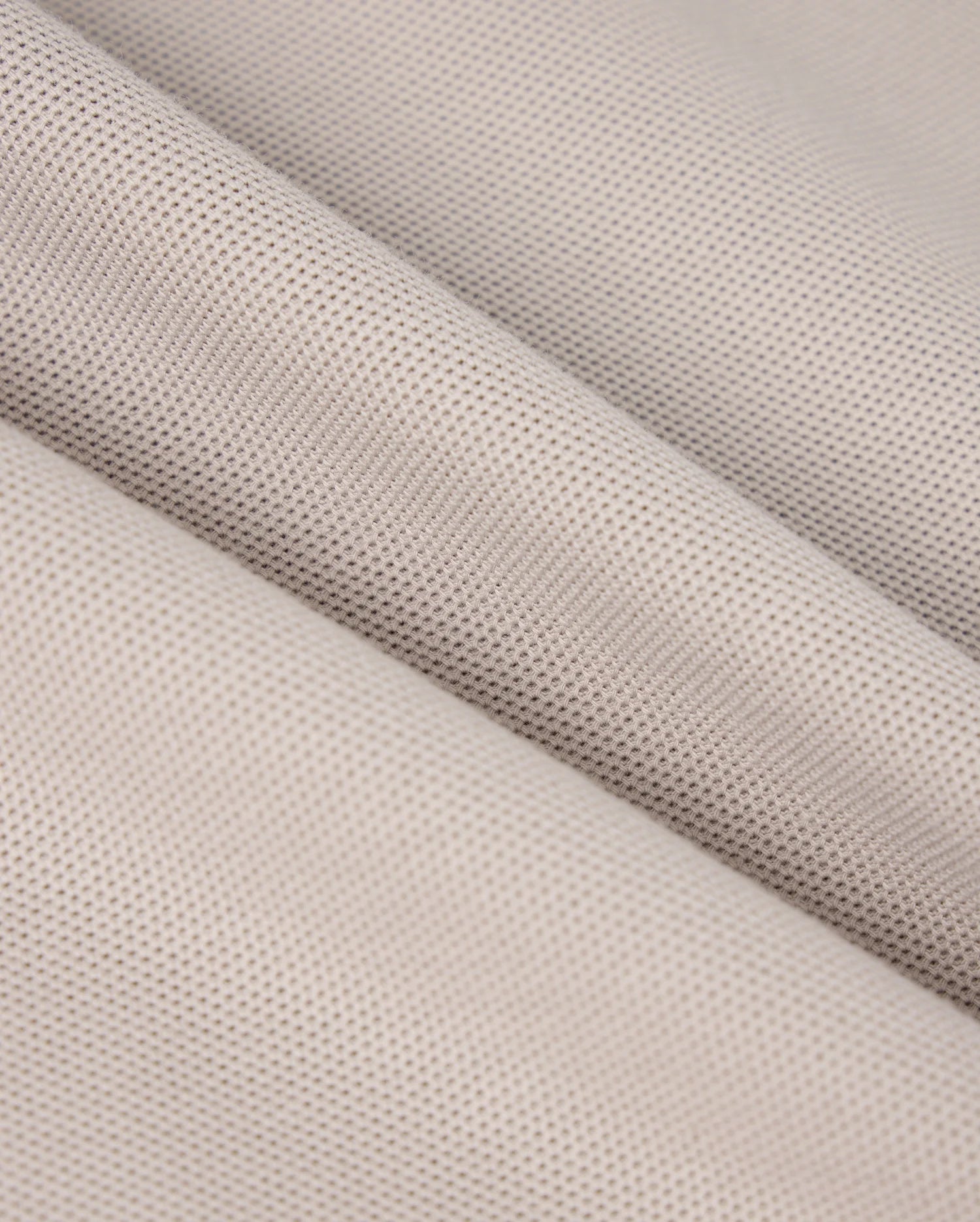 Close-up of a piece of light grey woven fabric with a fine, smooth texture. The fabric is draped to create gentle, diagonal folds, highlighting its soft and pliable nature, reminiscent of the exquisite feel found in Psycho Bunny's MENS MALTON PIQUE POLO SHIRT - B6K950D200.