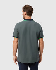 A man with brown hair is wearing a stylish Psycho Bunny polo in green, accented with black and green trim on the sleeves and collar. The MENS KENT PIQUE POLO SHIRT (B6K951D200), made from exquisite Pima cotton, exudes elegance as he stands facing away from the camera against a plain background.