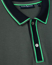Close-up of the stylish Men's Kent Pique Polo Shirt in dark green, featuring a black collar and neon green trim. This Psycho Bunny shirt showcases a two-button placket and a small tag near the collar with the brand name.