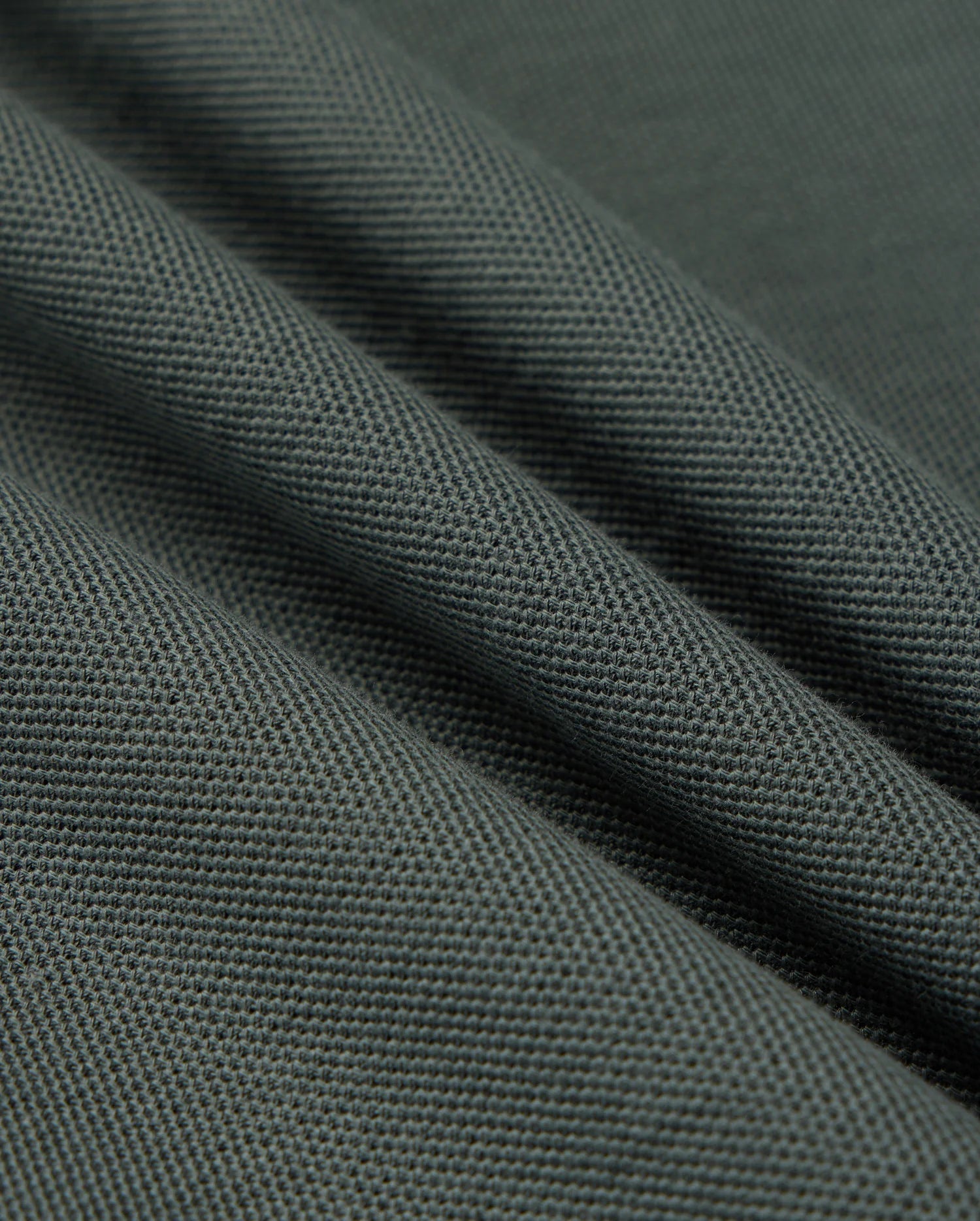 Close-up of the Psycho Bunny MENS KENT PIQUE POLO SHIRT in dark grey, featuring a textured weave pattern reminiscent of stylish polo fabric. The material is folded to form diagonal lines across the image, emphasizing its sturdy and dense quality.