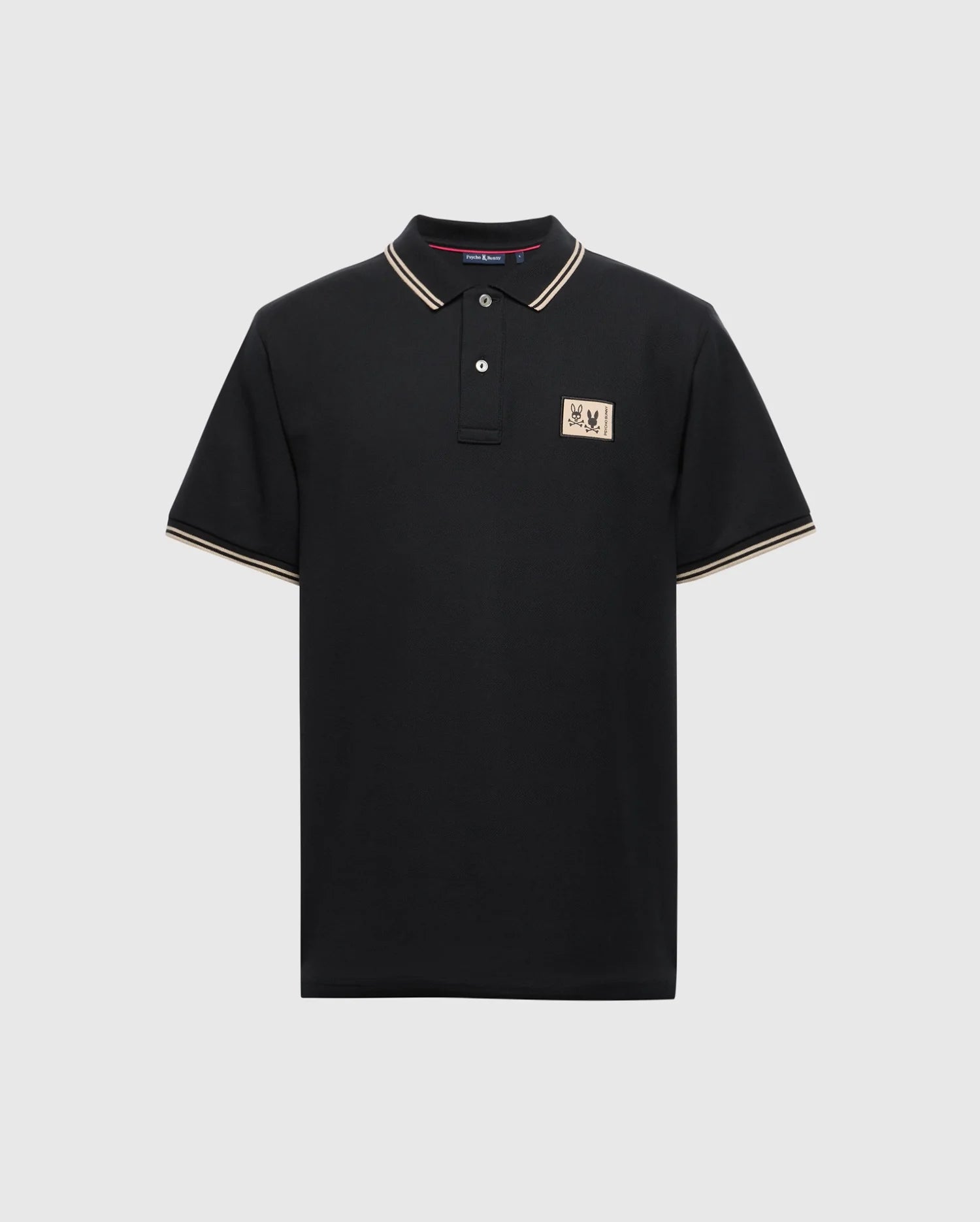 A Psycho Bunny Men's Monroe Pique Polo (B6K964D200) in black Pima cotton, designed with white and gold trim on the collar and sleeves. It includes a small beige patch with an emblem on the left chest and is complemented by three Mother-of-Pearl buttons along the placket, all set against a plain white background.