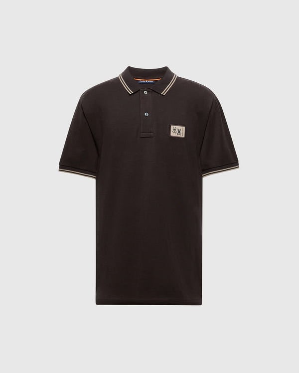 Psycho Bunny's MENS MONROE PIQUE POLO - B6K964D200 is a black Pima cotton polo shirt with beige trim on the collar and sleeves. It features a beige rectangular logo patch on the upper left chest and comes with a three-button placket adorned with Mother-of-Pearl buttons, displayed against a plain gray background.