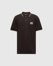 Psycho Bunny's MENS MONROE PIQUE POLO - B6K964D200 is a black Pima cotton polo shirt with beige trim on the collar and sleeves. It features a beige rectangular logo patch on the upper left chest and comes with a three-button placket adorned with Mother-of-Pearl buttons, displayed against a plain gray background.