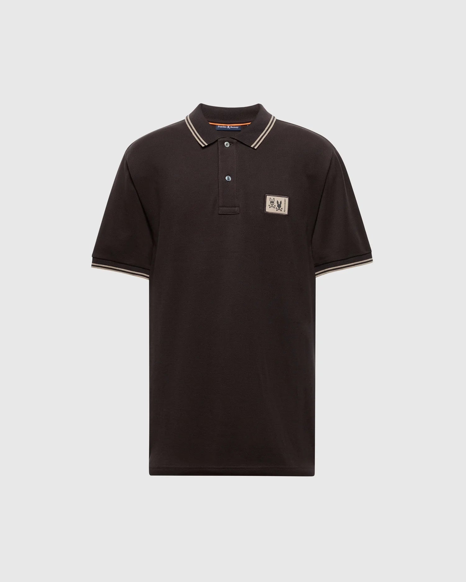 Psycho Bunny's MENS MONROE PIQUE POLO - B6K964D200 is a black Pima cotton polo shirt with beige trim on the collar and sleeves. It features a beige rectangular logo patch on the upper left chest and comes with a three-button placket adorned with Mother-of-Pearl buttons, displayed against a plain gray background.