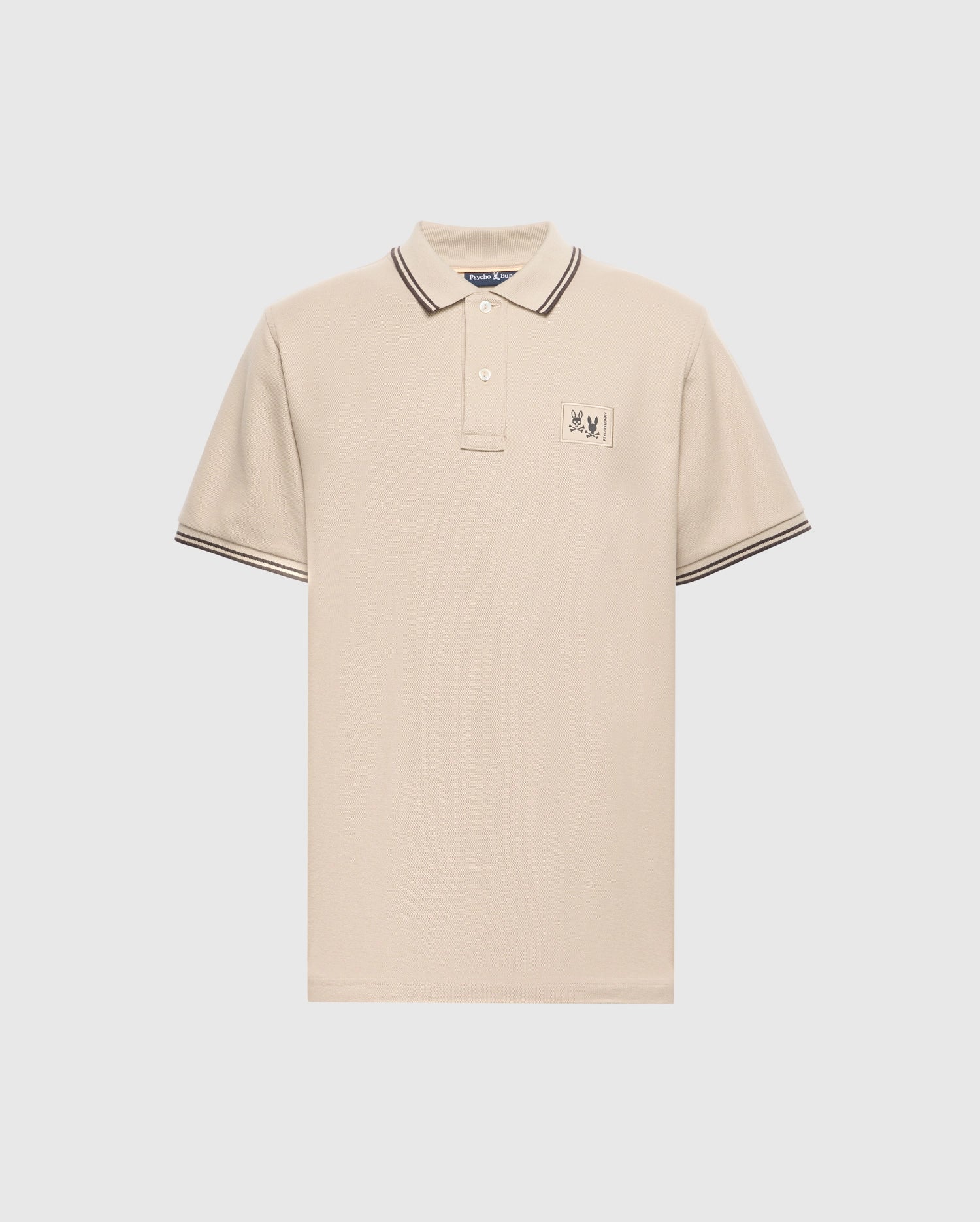 The Psycho Bunny Men's Monroe Pique Polo - B6K964D200 is a beige short-sleeve polo crafted from premium Pima cotton and made in Peru. It features a pointed collar with striped detailing, a two-button placket, and a small embroidered logo on the left chest for superior quality and comfort.