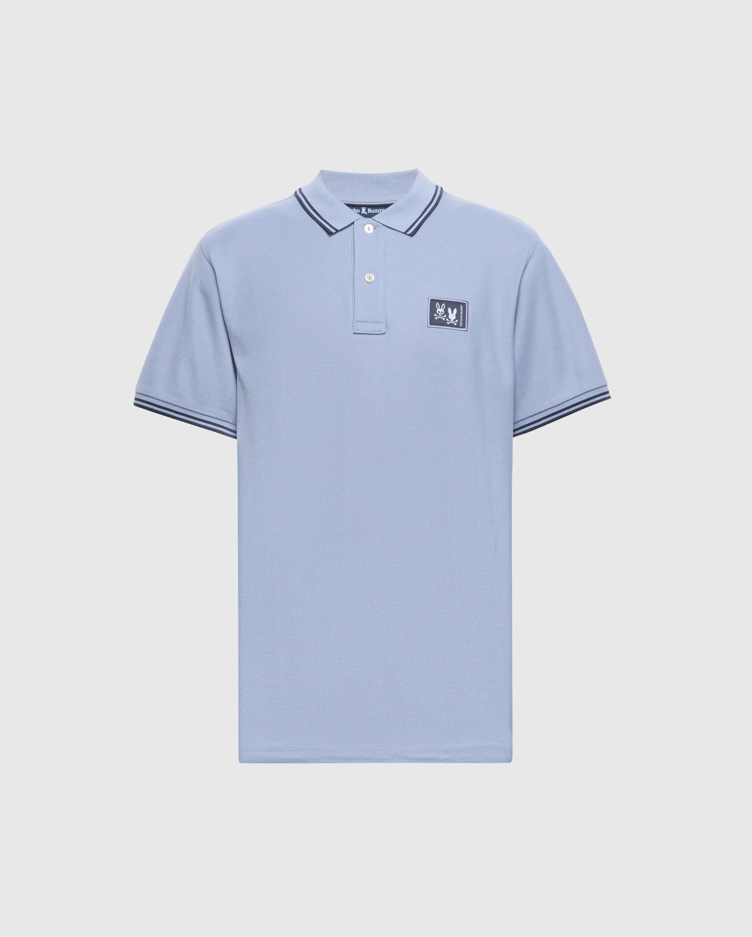 The Psycho Bunny MENS MONROE PIQUE POLO (B6K964D200) is a light blue Pima cotton polo with short sleeves, a buttoned collar, a chest embroidered patch, Mother-of-Pearl buttons, and black/white striped detailing on the collar and cuffs.