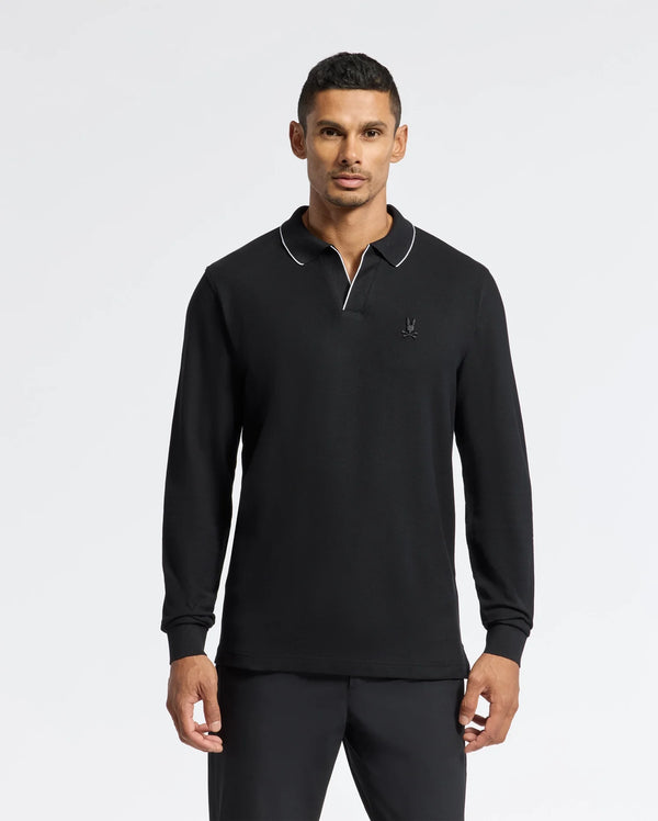 A man wearing a Psycho Bunny Men's Creede Pique Johnny Collar Polo - B6M265E200, featuring a Johnny collar with white piping at the neckline, stands against a plain white background. The black polo is crafted from soft Pima cotton and showcases a small embroidered logo on the left chest.