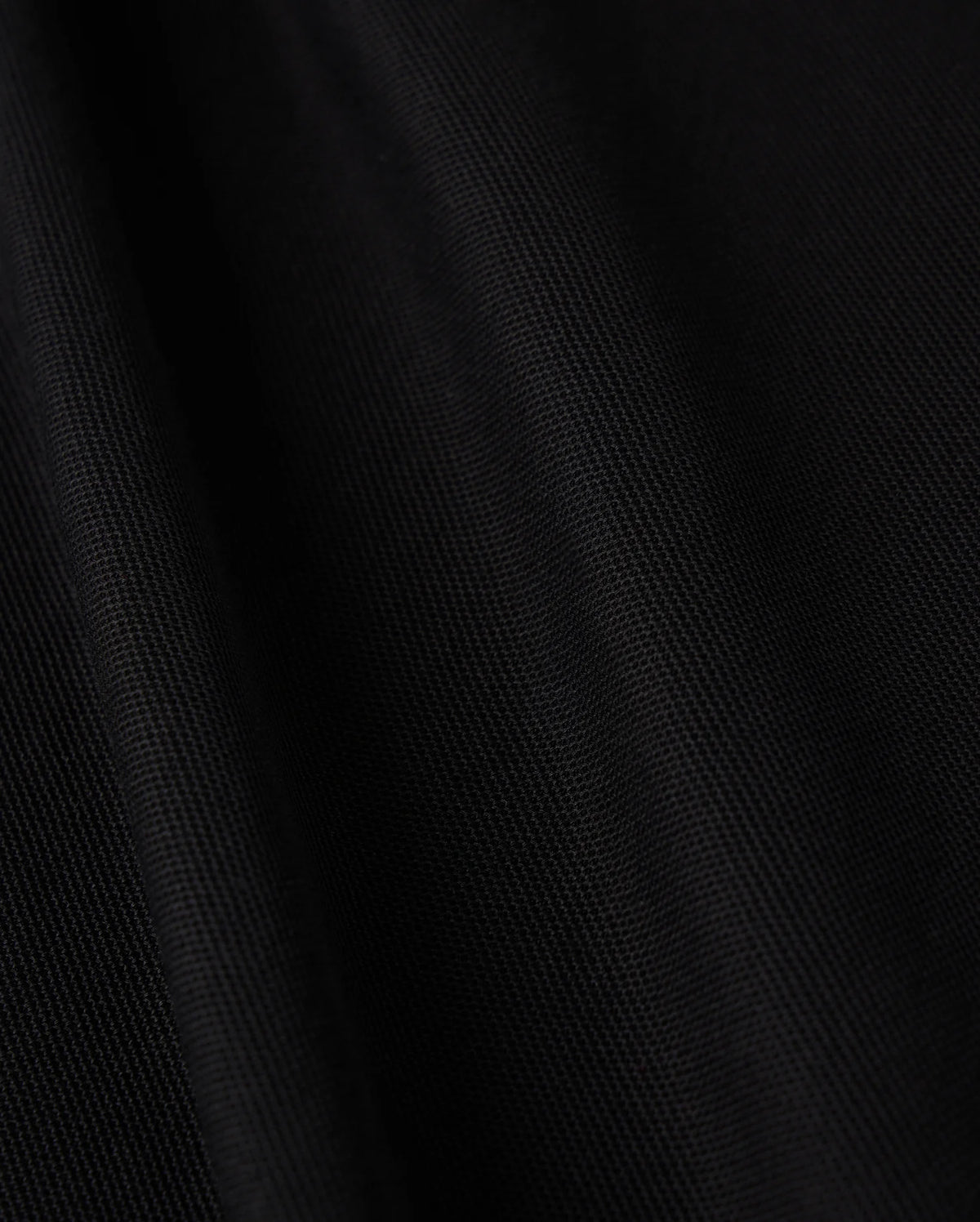 Close-up image of black Pima cotton fabric featuring a subtle diagonal texture, which gives it a smooth and sleek appearance. The lighting accentuates the folds, adding depth and a soft sheen to the material, making it ideal for crafting the sophisticated MENS KENT LONG SLEEVE PIQUE POLO by Psycho Bunny (B6M935D200).