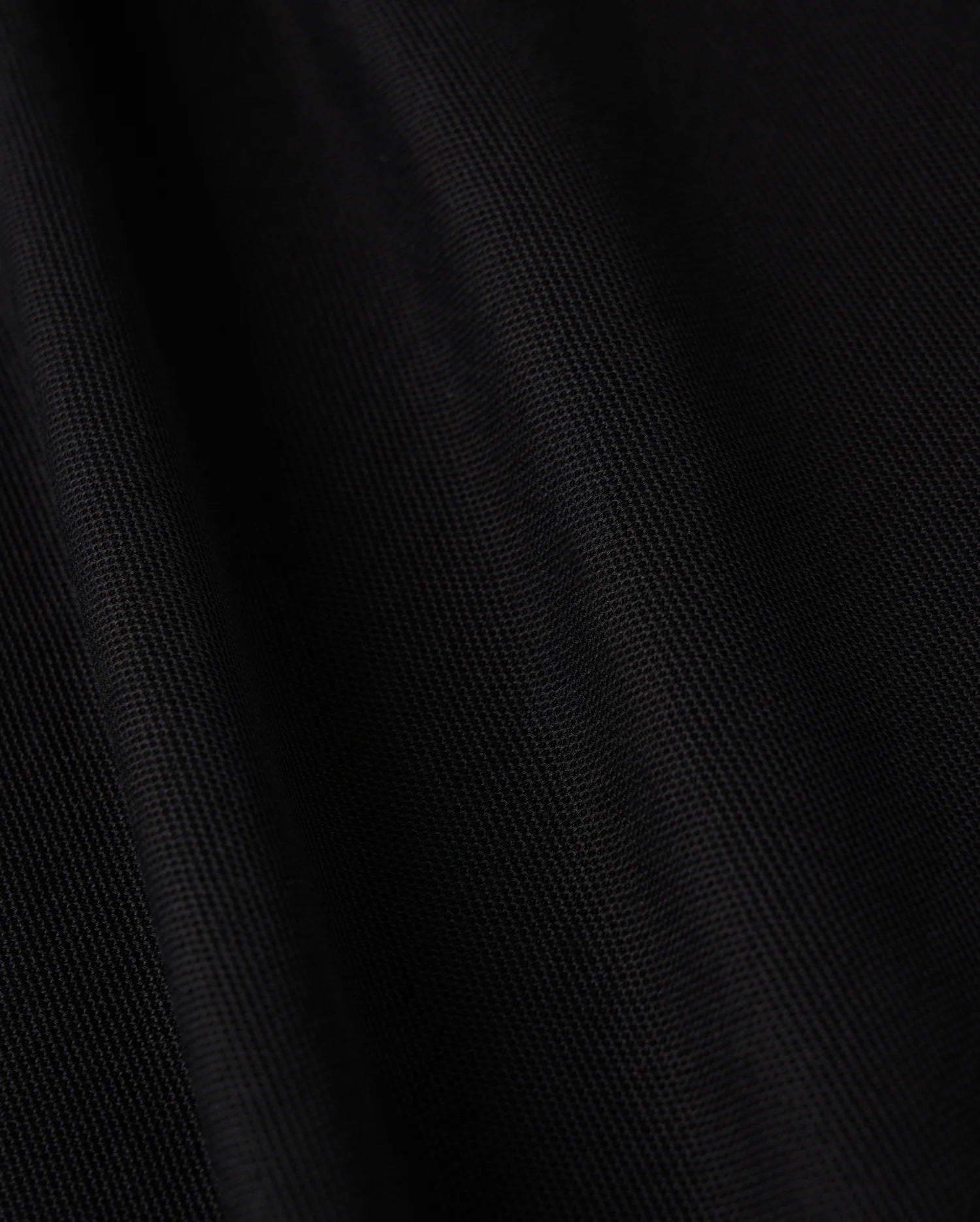 Close-up image of black Pima cotton fabric featuring a subtle diagonal texture, which gives it a smooth and sleek appearance. The lighting accentuates the folds, adding depth and a soft sheen to the material, making it ideal for crafting the sophisticated MENS KENT LONG SLEEVE PIQUE POLO by Psycho Bunny (B6M935D200).