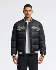 A man confidently wears the MENS FRAZER FASHION PUFFER - B6N338E200 from Psycho Bunny, showcasing its black design with "Psycho Bunny" embroidered on the chest. This fashionable piece is accented with white stripes on the collar, cuffs, and hem as he poses against a plain white background.