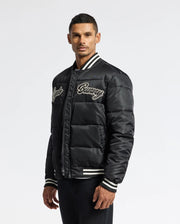 A man wearing the Psycho Bunny MENS FRAZER FASHION PUFFER, featuring white striped cuffs and embroidered text on the chest, stands against a plain background, looking at the camera.