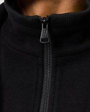 Close-up of the Psycho Bunny MENS STAFFORD WOOL BLEND COAT - B6N551D200 with a partially closed zipper displaying the logo. The soft, warm black wool blend fabric is ideal for chilly days against a plain background.