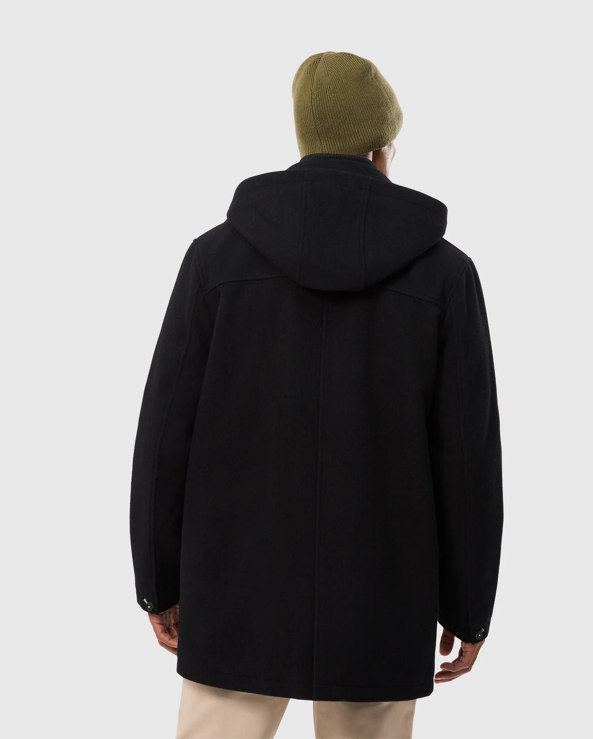 A person in an elegant Psycho Bunny MENS STAFFORD WOOL BLEND COAT - B6N551D200 and a green beanie stands with their back to us. The black coat contrasts with their light-colored pants against a plain, light gray background.