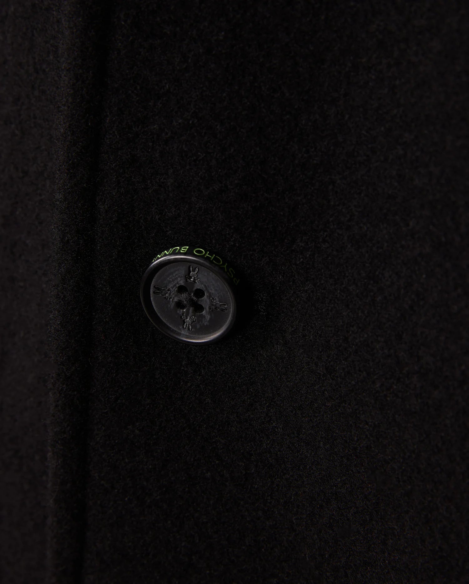 Zoom in on the refined black button of the Psycho Bunny Men's Stafford Wool Blend Coat - B6N551D200. This elegant winter coat boasts a four-hole button with discreet text around it and its wool blend fabric offers a soft, slightly textured look.