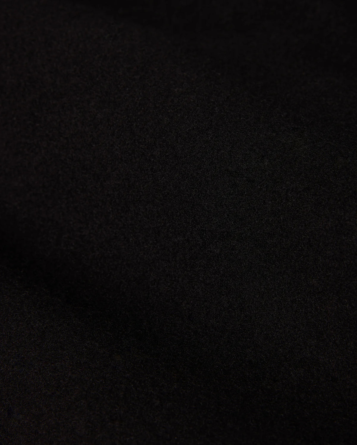 A close-up of the dark, textured fabric from the MENS STAFFORD WOOL BLEND COAT - B6N551D200 by Psycho Bunny reveals a soft, matte finish. The dense, finely woven material displays subtle shading variations due to lighting.