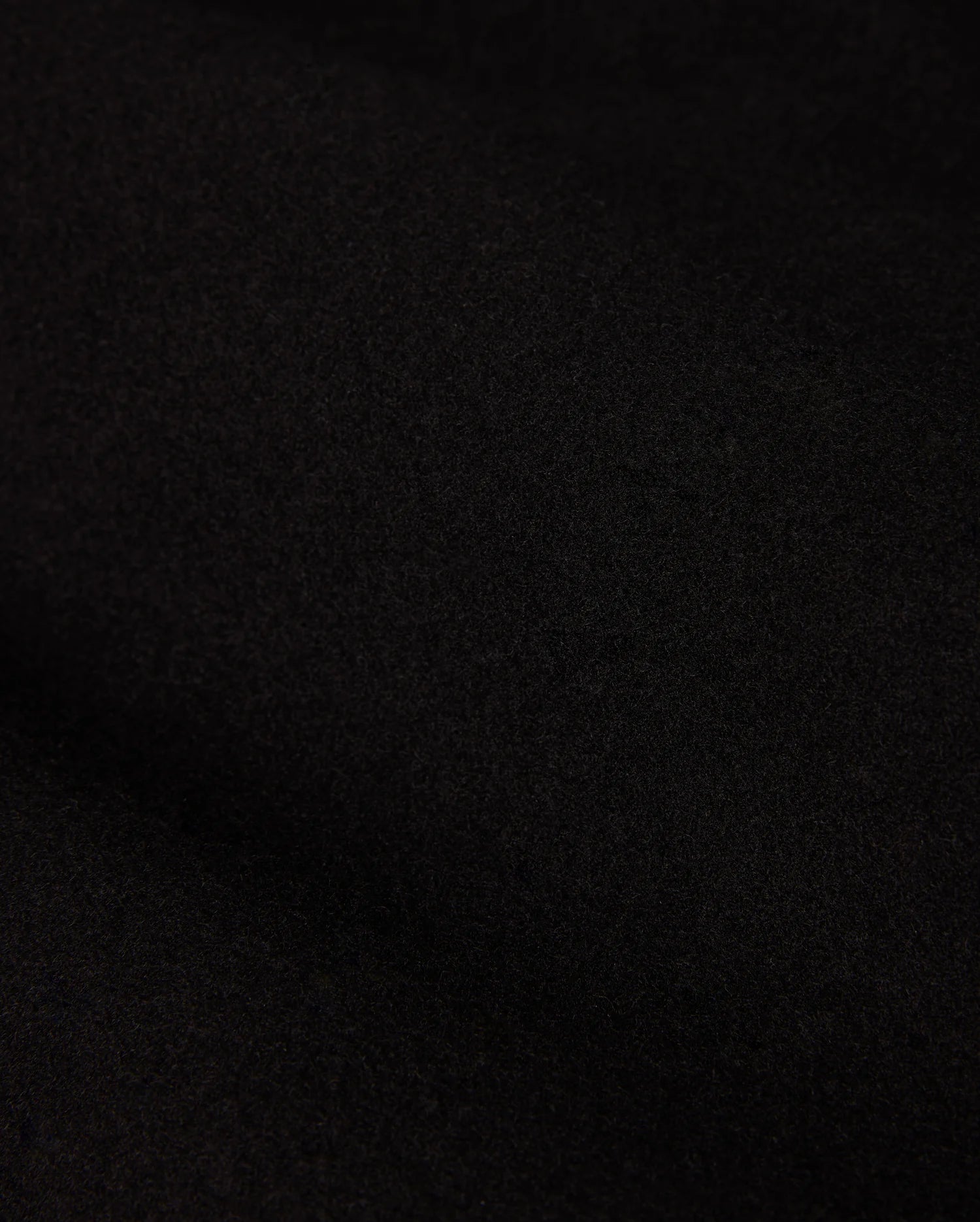 A close-up of the dark, textured fabric from the MENS STAFFORD WOOL BLEND COAT - B6N551D200 by Psycho Bunny reveals a soft, matte finish. The dense, finely woven material displays subtle shading variations due to lighting.