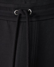 Close-up of black Psycho Bunny MENS TRAVIS TRACK PANT - B6P143D200 featuring a drawstring waistband. The drawstrings are threaded through metal eyelets, and the high-quality cotton-blend fabric has a smooth, slightly textured appearance. The stitching and seams are visible, showcasing the garment's craftsmanship.