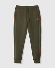 The MENS TRAVIS TRACK PANT - B6P143D200 by Psycho Bunny is crafted from a high-quality cotton blend in an olive green hue, featuring distinctive orange piping along the sides. These pants come with an elastic waistband complete with a drawstring, side invisible zip pockets, and cuffed ankles for added comfort and style. A small embroidered logo adorns the left thigh. Displayed against a plain white background.
