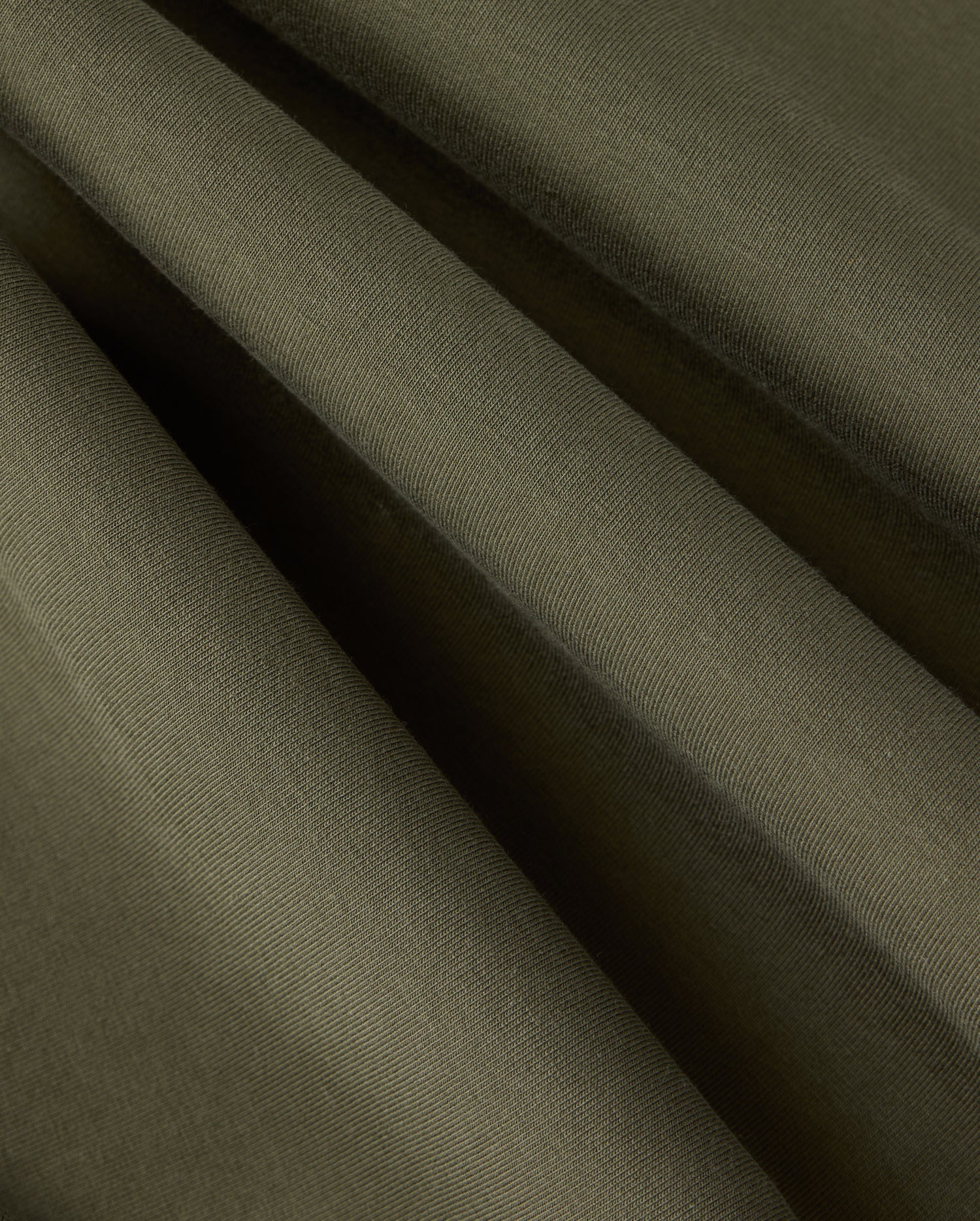 Close-up view of folded dark green fabric with visible texture and subtle shadows, showcasing the smooth surface and soft draping folds of high-quality cotton-blend material found in the Psycho Bunny MENS TRAVIS TRACK PANT - B6P143D200.