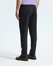 A person is standing and facing away, wearing the MENS ALEXANDER SWEATPANT - B6P155E200 by Psycho Bunny along with black shoes. The background appears light, and their left arm is partially visible. The cotton sweatpants include a pocket on the back.