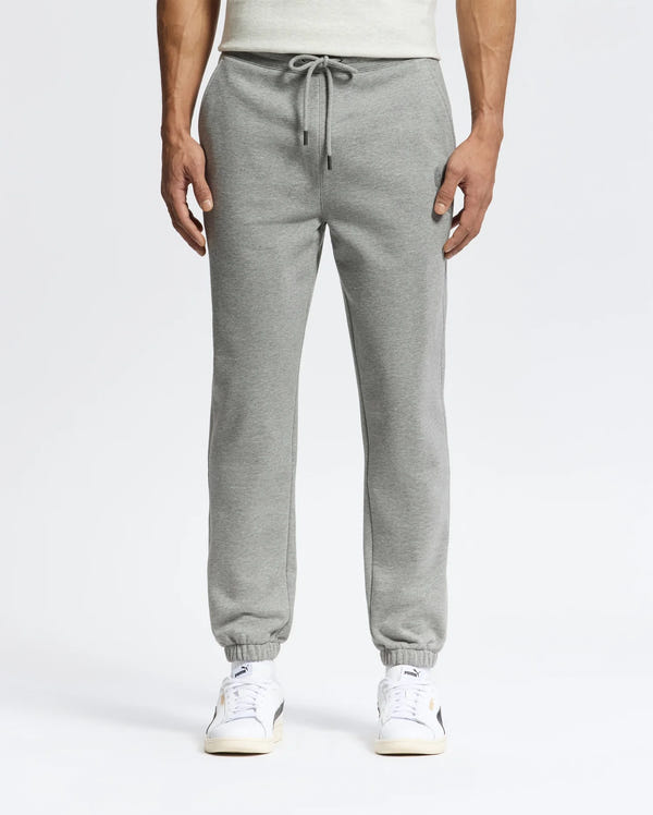 A person in sleek Psycho Bunny MENS ELDORADO BRUSH BACK JOGGER - B6P285E200, featuring a drawstring, elastic cuffs, side pockets, and brushback comfort, stands against a plain backdrop. They pair the joggers with white sneakers with beige soles.