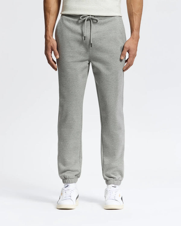 A person in sleek Psycho Bunny MENS ELDORADO BRUSH BACK JOGGER - B6P285E200, featuring a drawstring, elastic cuffs, side pockets, and brushback comfort, stands against a plain backdrop. They pair the joggers with white sneakers with beige soles.