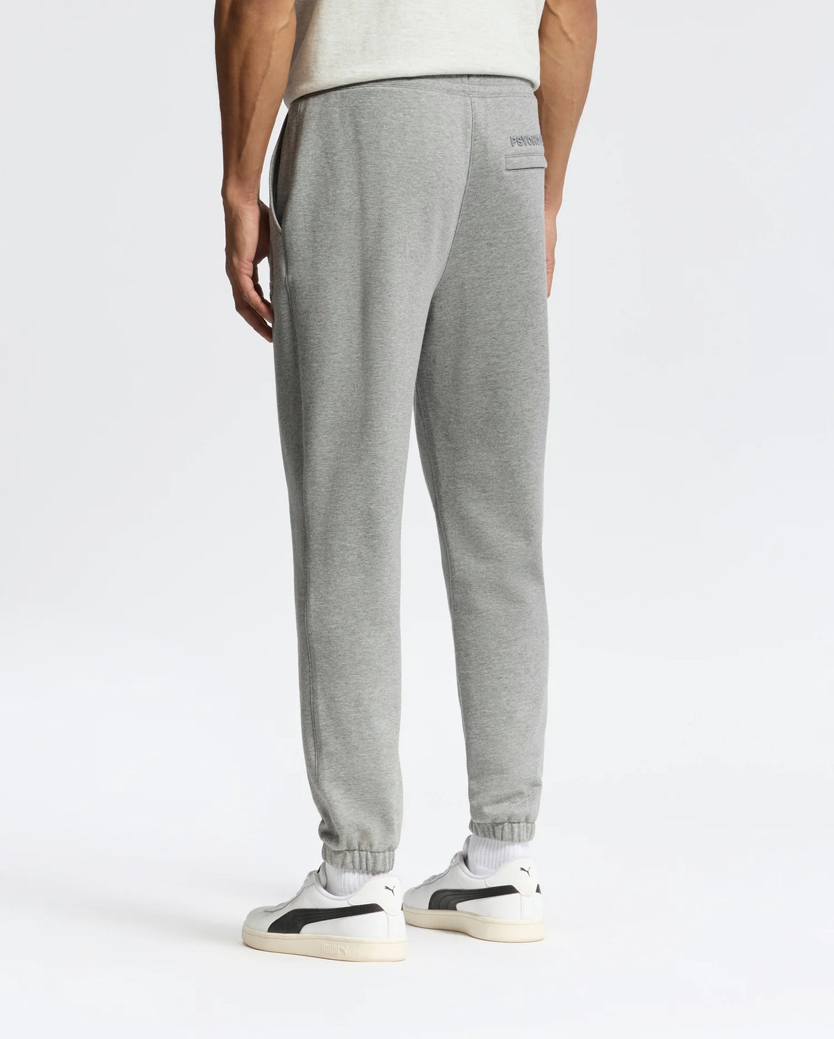 Wearing Psycho Bunny's sleek MENS ELDORADO BRUSH BACK JOGGER - B6P285E200 in gray, a person stands against a plain white background, paired with white sneakers. They face away, highlighting the small logo on the upper back pocket area.
