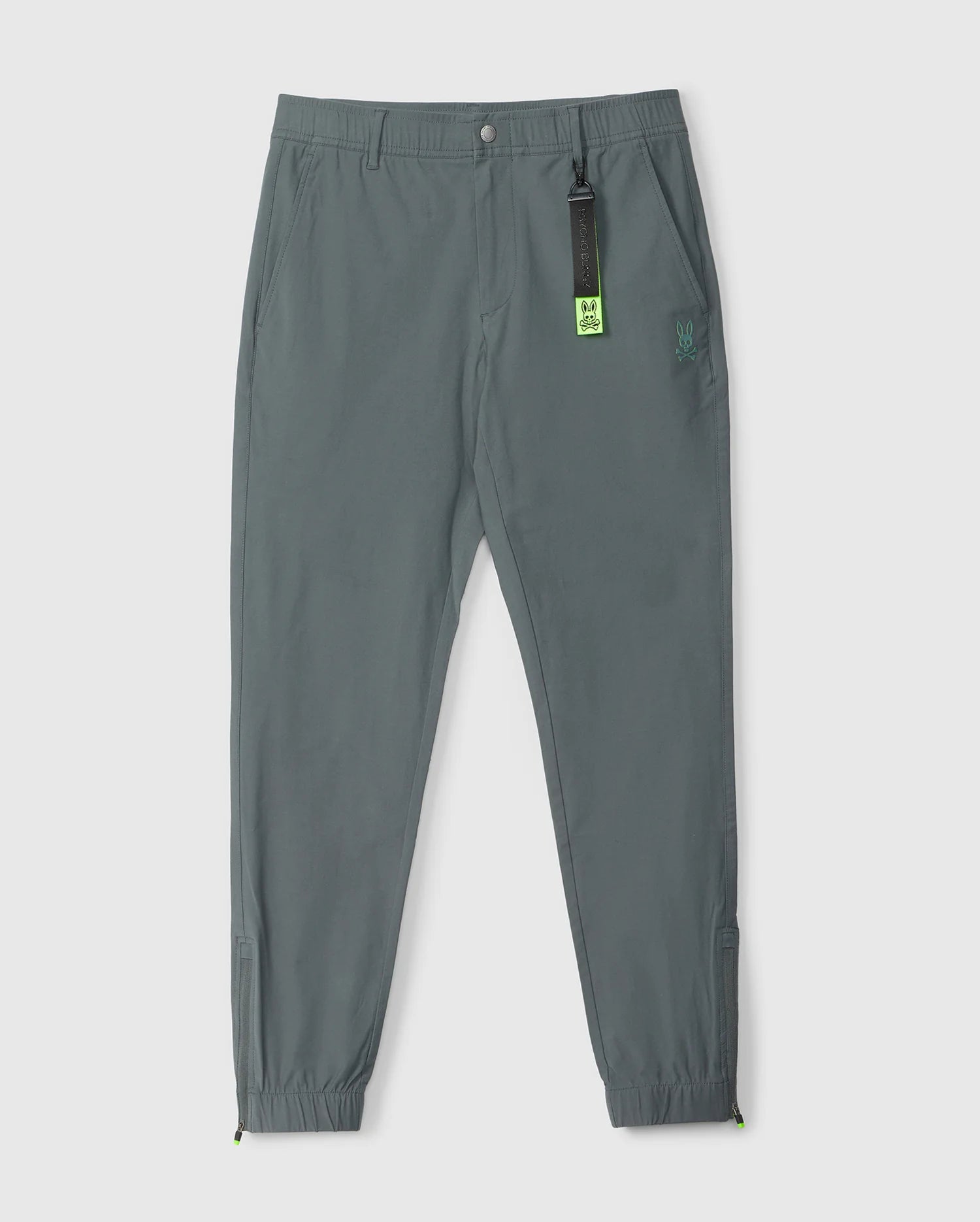 Gray jogger pants with elastic cuffs, an elasticized waistband, and a small Psycho Bunny logo on the left thigh. A neon green Psycho Bunny tag is attached to the waistband. The background is plain white.