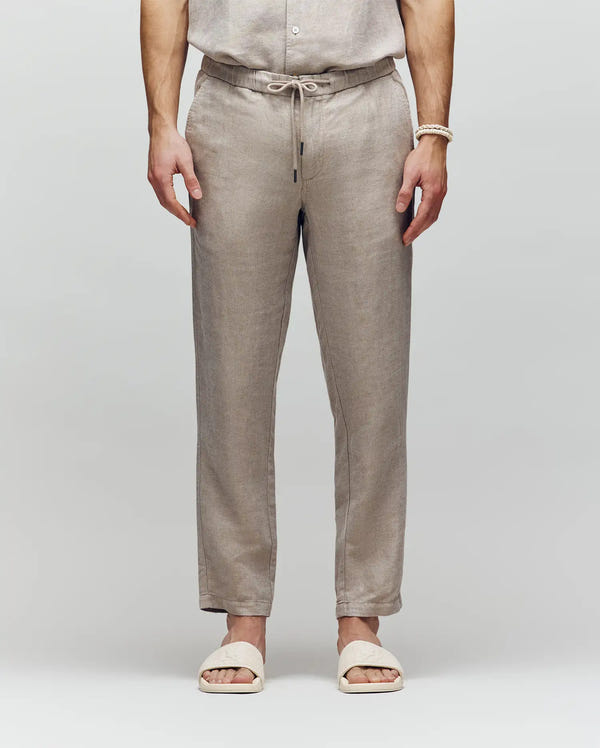 A person wears Psycho Bunny MENS FATE LINEN DRAWSTRING PANT (B6P471C200) and cream slide sandals, standing with hands relaxed at their sides against a plain light background.
