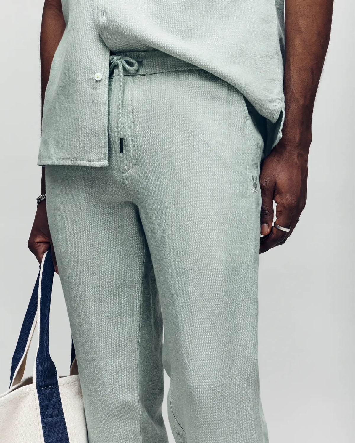 Psycho Bunny linen pants in light green, featuring a drawstring waist, relaxed fit, visible linen texture, and a small embroidered bunny skull logo on the front pocket.