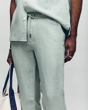 Psycho Bunny linen pants in light green, featuring a drawstring waist, relaxed fit, visible linen texture, and a small embroidered bunny skull logo on the front pocket.
