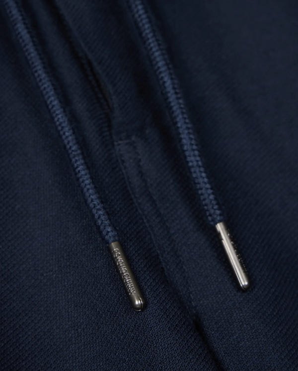 Close-up of navy blue drawstrings with silver metal tips on a dark fabric background, perfect for the Psycho Bunny MENS FATE LINEN DRAWSTRING PANT - B6P471C200. The metal tips have small engraved text, but the content is not fully readable in the image. Ideal for those summer trousers that need both style and durability.