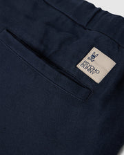 Close-up of the back pocket of MENS FATE LINEN DRAWSTRING PANT - B6P471C200 by Psycho Bunny. The black summer trousers feature a beige tag with a bunny face logo and crossbones underneath, along with the text "Psycho Bunny.